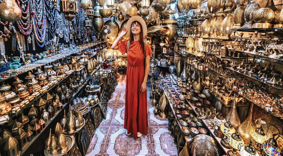 Person in a red dress and hat stands in a vibrant shop filled with intricate metal lanterns and decorative items.