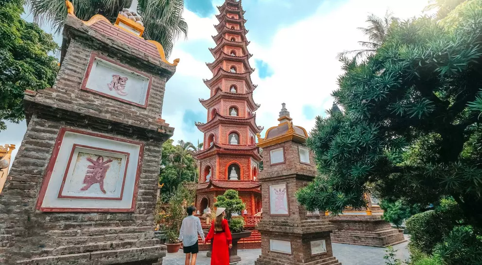 Couple walking towards a tall pagoda surrounded by greenery and traditional stone structures.