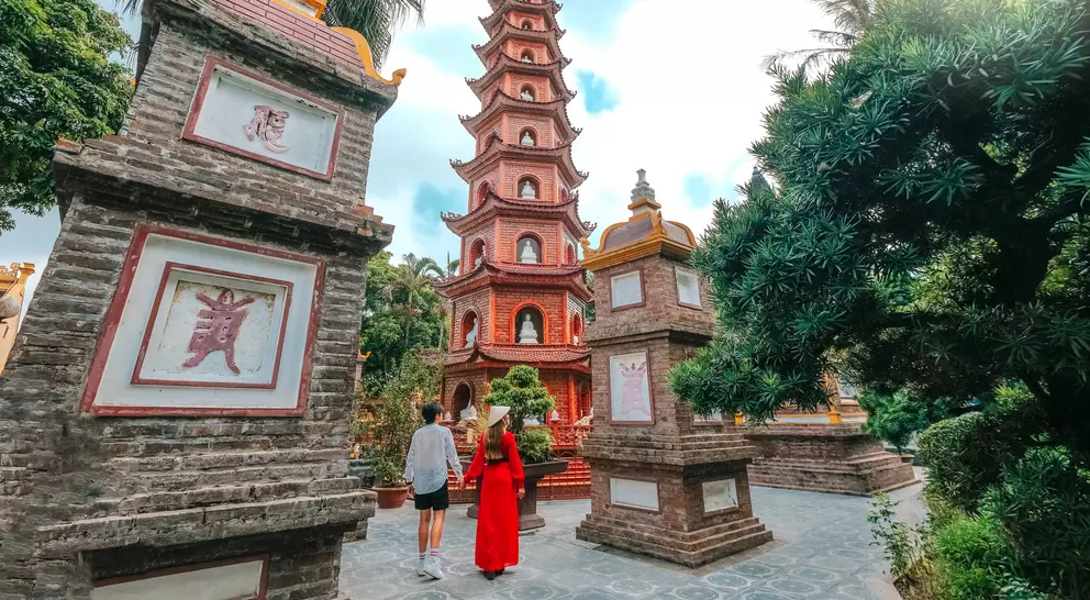 Couple walking towards a tall pagoda surrounded by greenery and traditional stone structures.