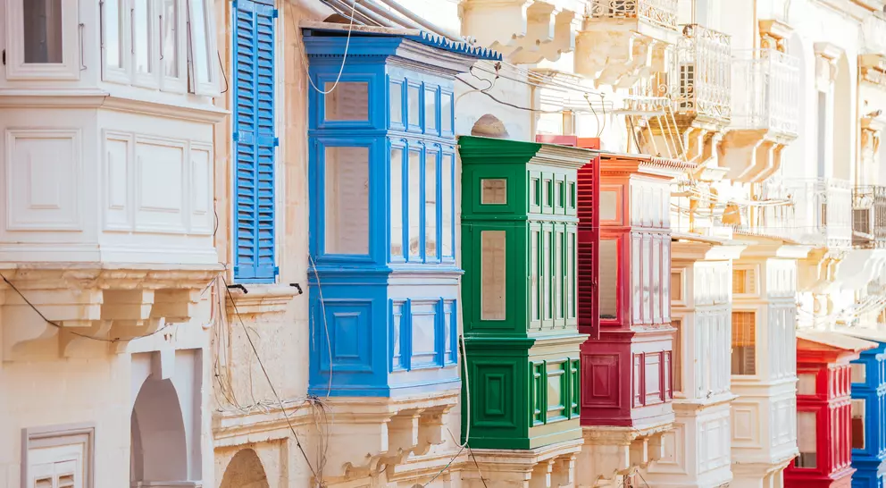 Colorful balconies in blue, green, red, and white line a narrow street, showcasing vibrant architectural details.