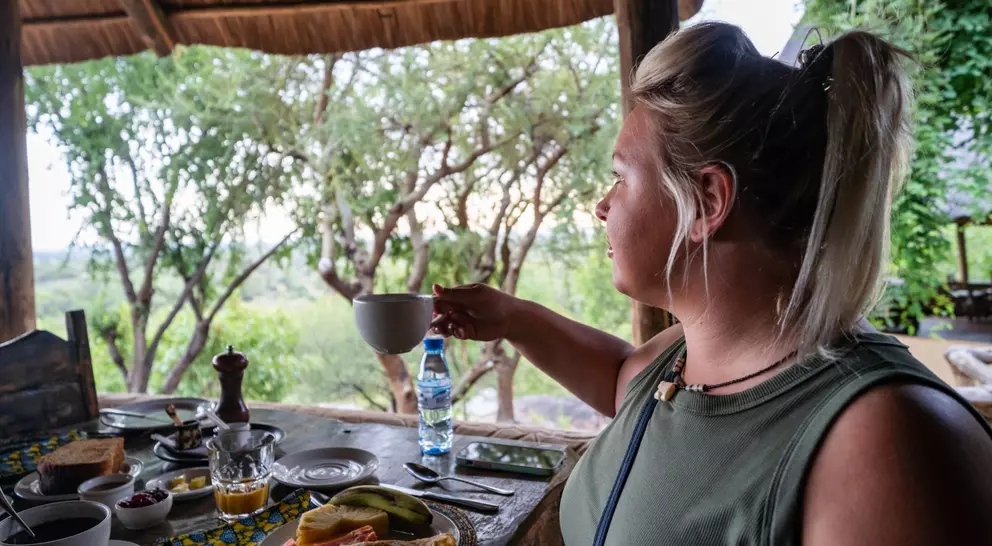 A person enjoying breakfast with fruits and drinks at an outdoor table, overlooking a scenic green landscape.