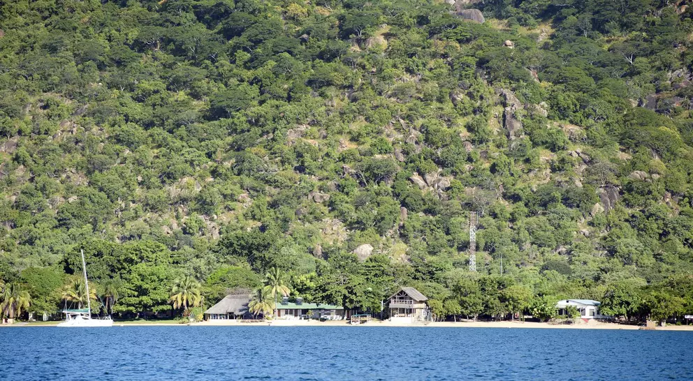 A panoramic view of Lake Malawi, Africa. The lake is surrounded by lush green hills and has crystal-clear blue water.