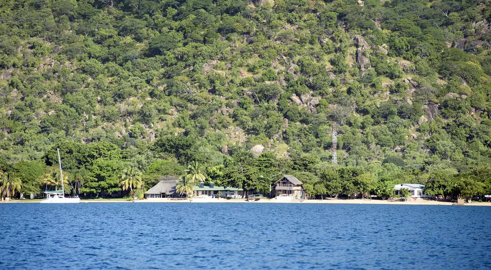 A panoramic view of Lake Malawi, Africa. The lake is surrounded by lush green hills and has crystal-clear blue water.