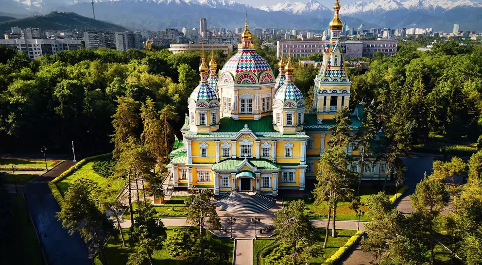 Aerial view of the Zenkov Cathedral in Panfilov Park against blue sky and and snowy mountains in Almaty city, Kazakhstan