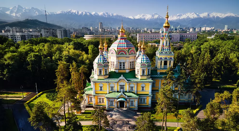 Aerial view of the Zenkov Cathedral in Panfilov Park against blue sky and and snowy mountains in Almaty city, Kazakhstan