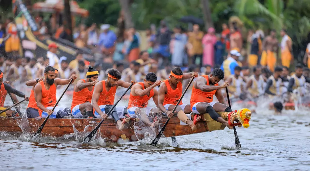 A team of rowers in orange shirts paddles a dragon boat, competing in a race with a large crowd watching.