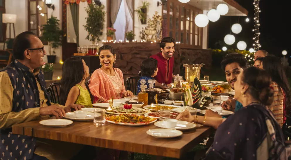A festive outdoor dinner with several people enjoying food, laughing, and celebrating under soft lighting.