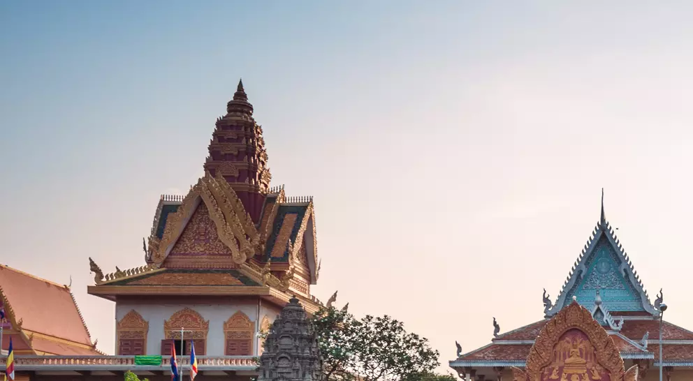 Traffic scene with rickshaws and motorbikes near a colorful temple complex at sunset.