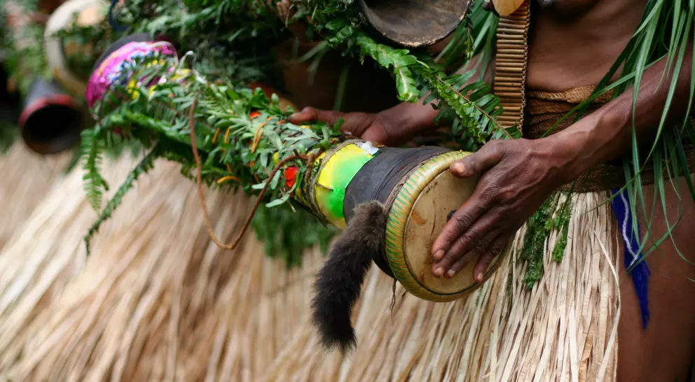 Woman beating a hand-made drum as part of a tribal ceremony. Papua New Guinea.