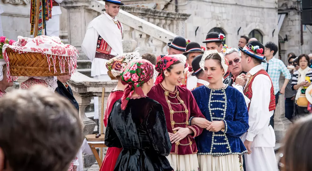 Group of people in traditional costumes at a cultural event, engaged in conversation, with a festive atmosphere.