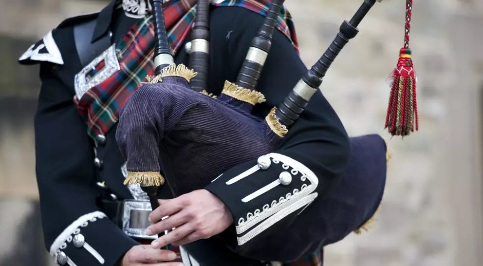 Close up of the hands of a Scottish bagpiper clad in a traditional scottish tartan playing the Scottish bagpipe