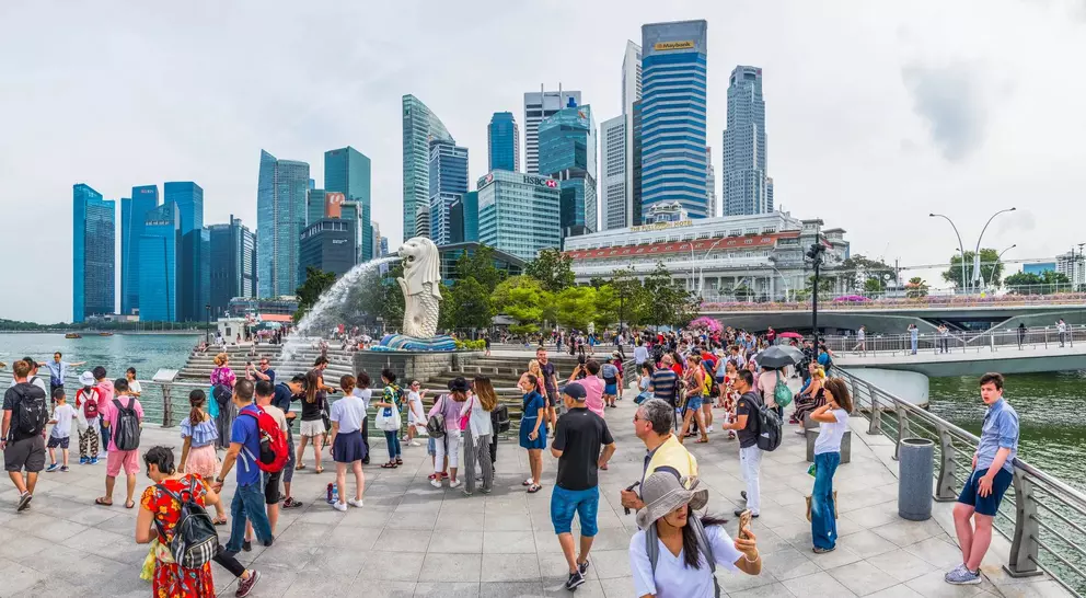 Crowd gathered by the Merlion statue with Singapore's skyline in the background, featuring modern skyscrapers.