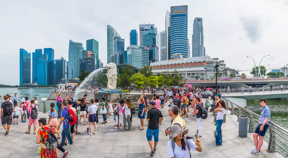 Crowd gathered by the Merlion statue with Singapore's skyline in the background, featuring modern skyscrapers.