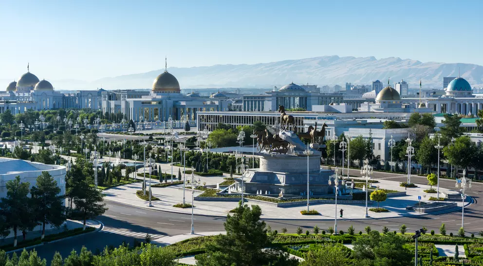 Panoramic view of a city with modern architecture, a large monument, and mountains in the background under clear blue skies.