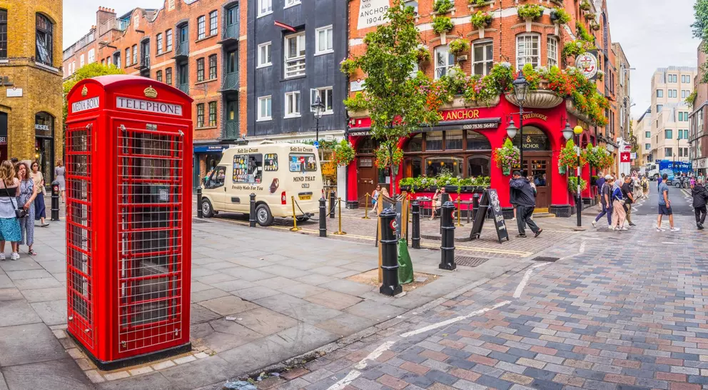 A vibrant street scene featuring a red telephone box, a pub adorned with flowers, and people enjoying the urban atmosphere.