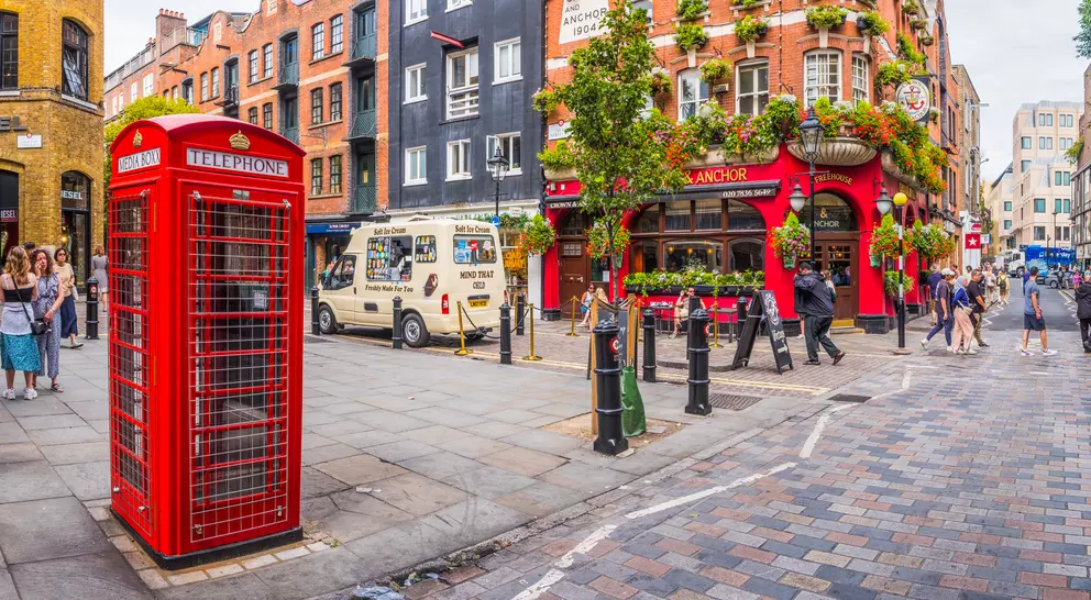 A vibrant street scene featuring a red telephone box, a pub adorned with flowers, and people enjoying the urban atmosphere.