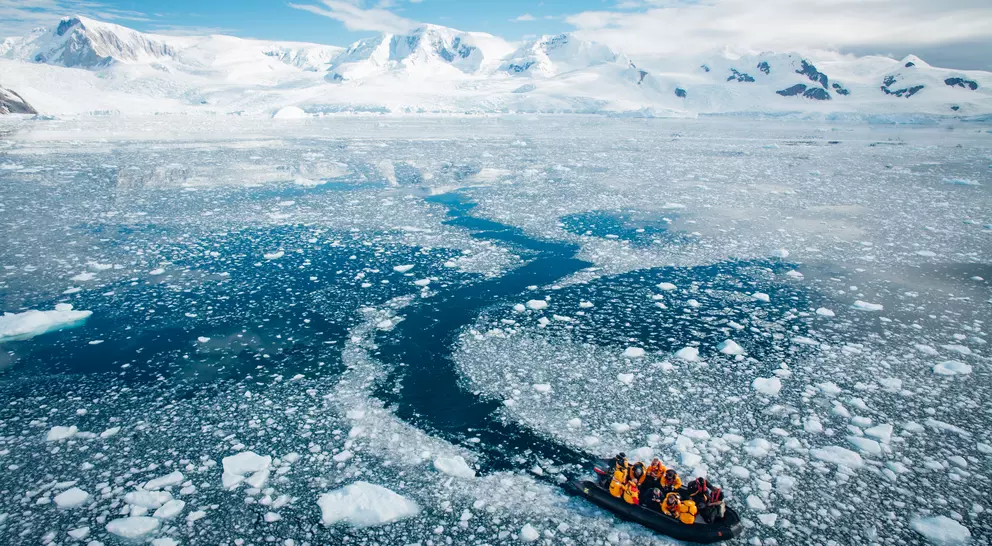 A small boat navigates through icy waters with snow-capped mountains in the background.