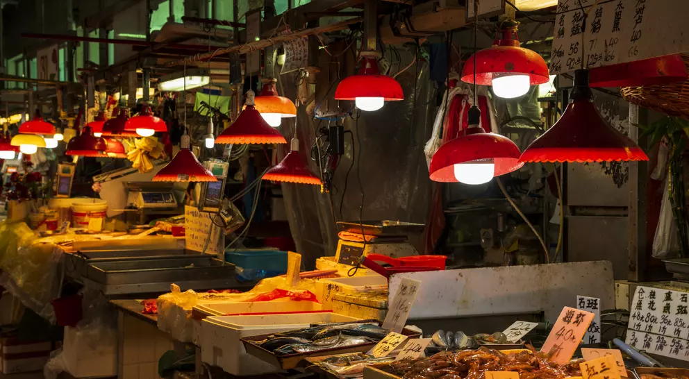 A bustling market stall with red lamps illuminating fresh seafood and produce, surrounded by vibrant signboards.