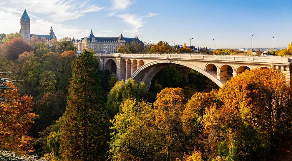 Scenic view of an arched bridge surrounded by colorful autumn trees and historic buildings against a blue sky.