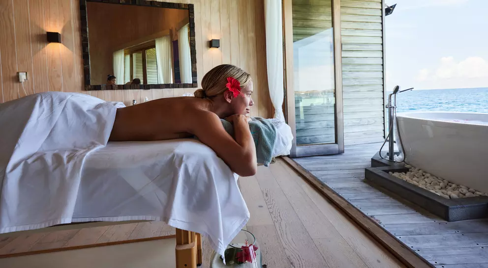 A person enjoys a relaxing massage in a serene spa with a view of the ocean, adorned with a flower in their hair.