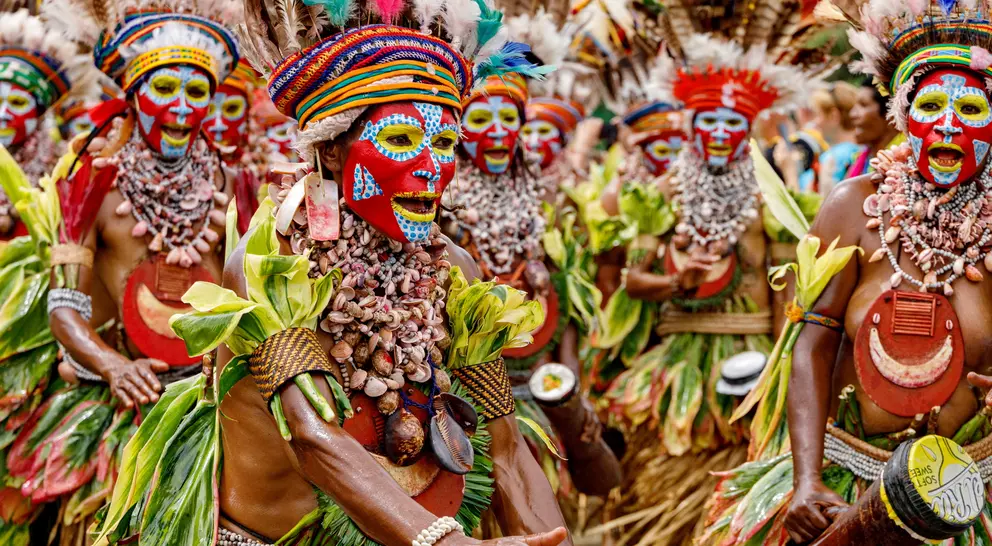 Indigenous dancers in vibrant costumes and face paint perform during a cultural celebration, surrounded by colorful decor.