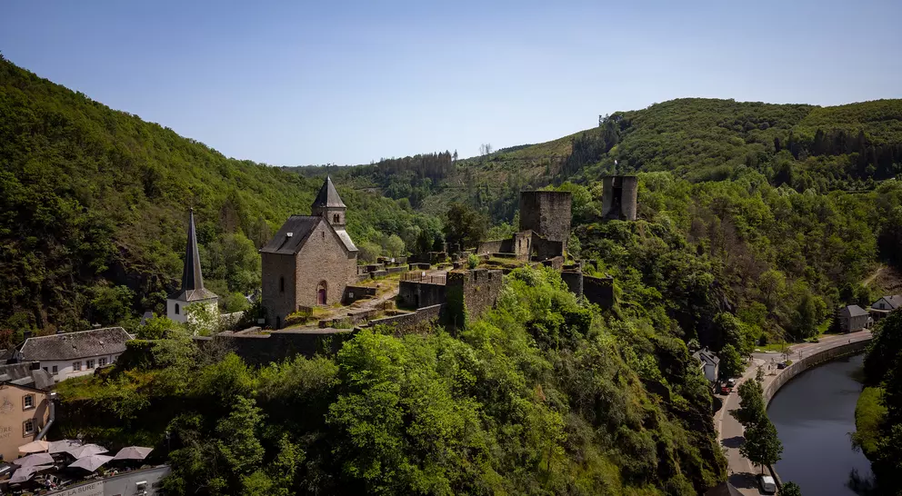 A medieval castle on a hill surrounded by lush greenery, overlooking a winding river and nearby village.