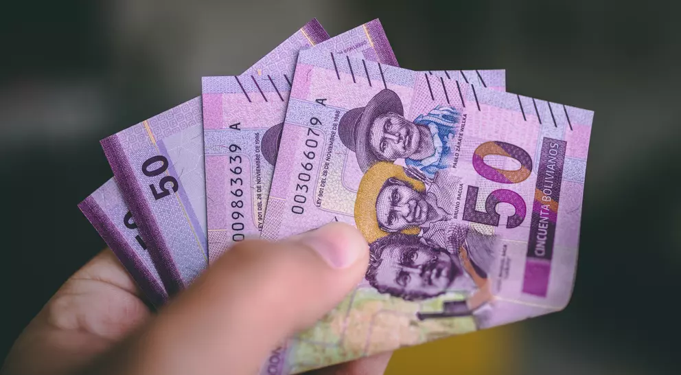 A hand holds several 50-unit banknotes featuring portraits of people, with purple and green designs.