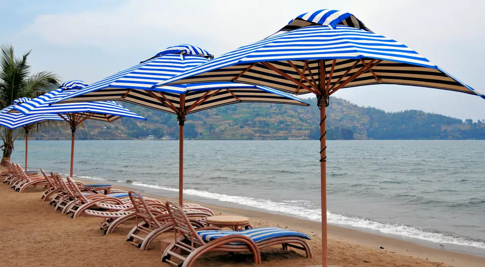 Row of blue and white striped beach umbrellas on sandy shore, with lounge chairs and calm sea in the background.