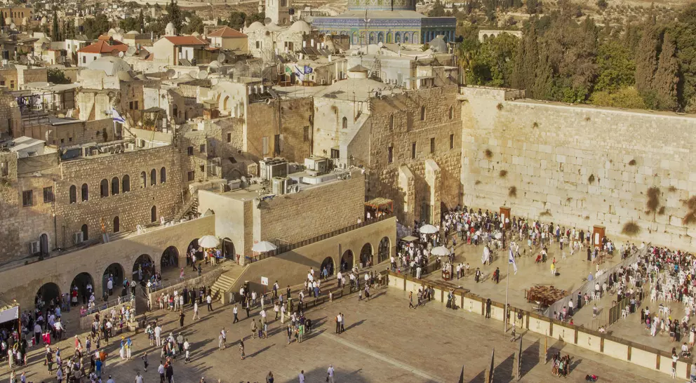 Aerial view of the Western Wall and the Dome of the Rock in Jerusalem, bustling with people and surrounded by historic buildings.