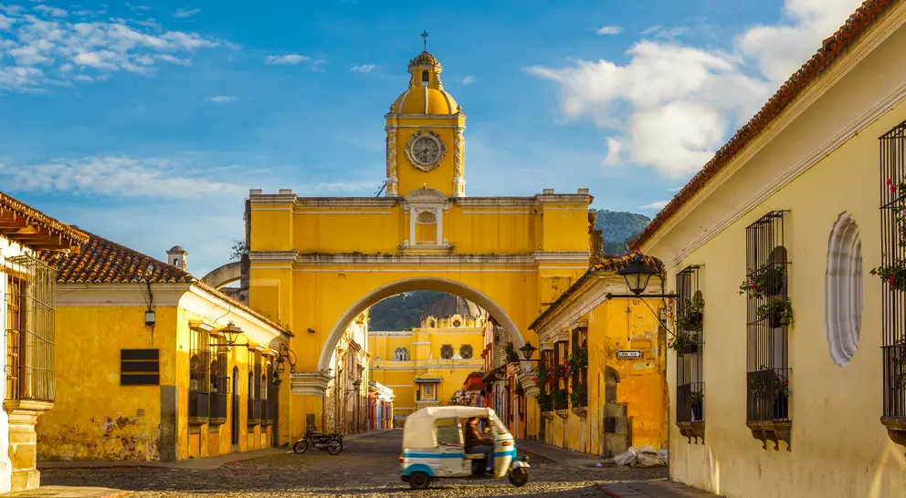 A tuk-tuk taxi passes in from of The Arch of Santa Catalina in Antigua, Guatemala