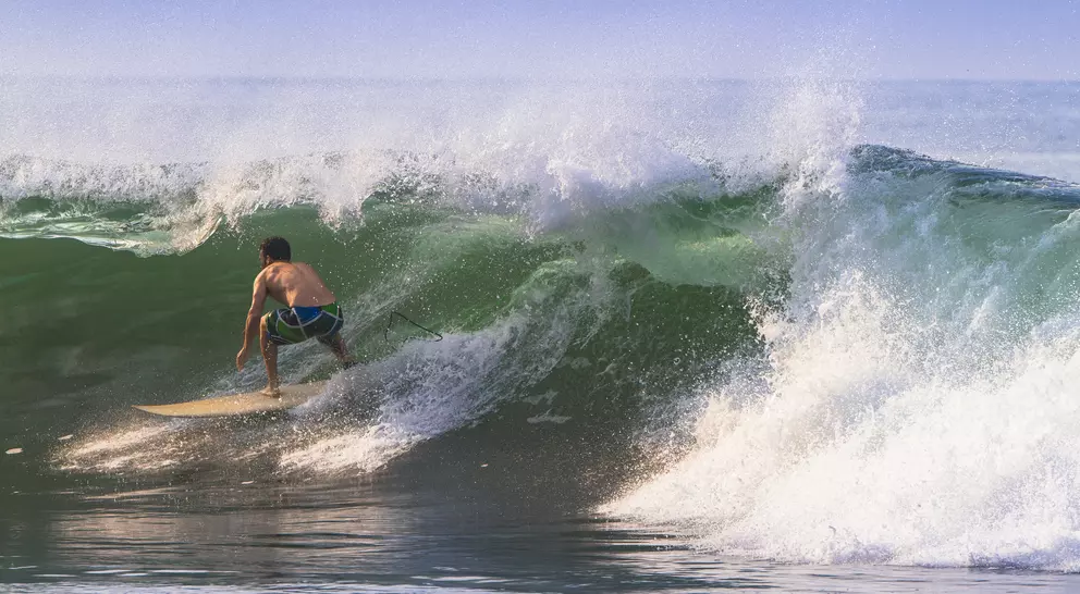 A surfer rides a large wave, skillfully maneuvering on his board as the water crashes around him.