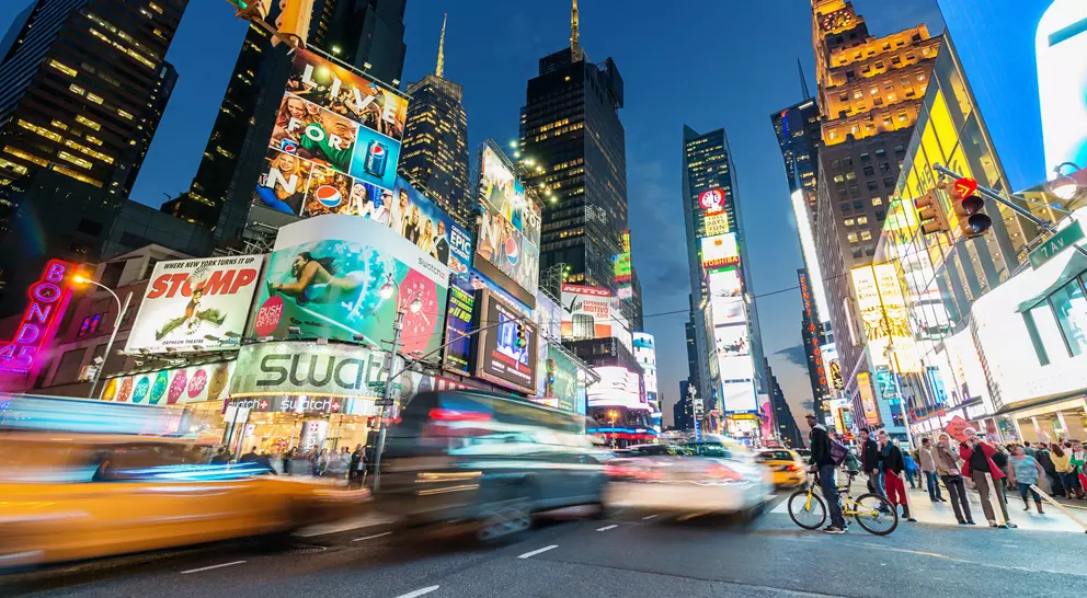 Brightly lit Times Square at dusk, with bustling traffic, pedestrians, and iconic billboards.