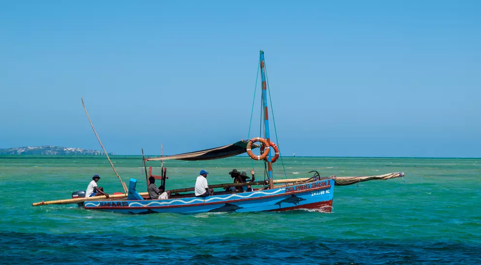 A colorful fishing boat with several people on the water, surrounded by a bright blue sky and clear green sea.