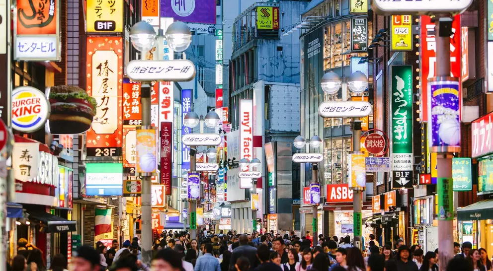 Busy street scene in a city, illuminated by colorful signs and bustling with people.