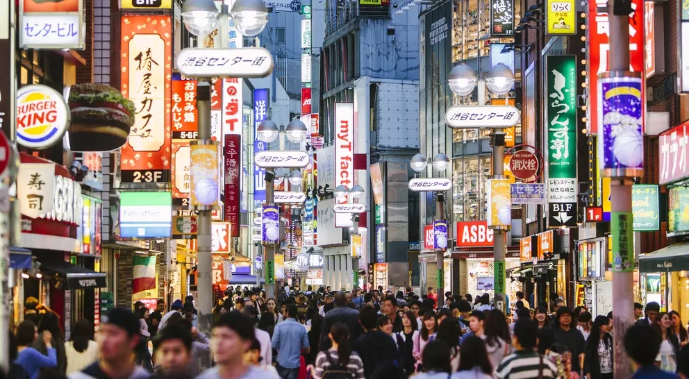 Busy street scene in a city, illuminated by colorful signs and bustling with people.