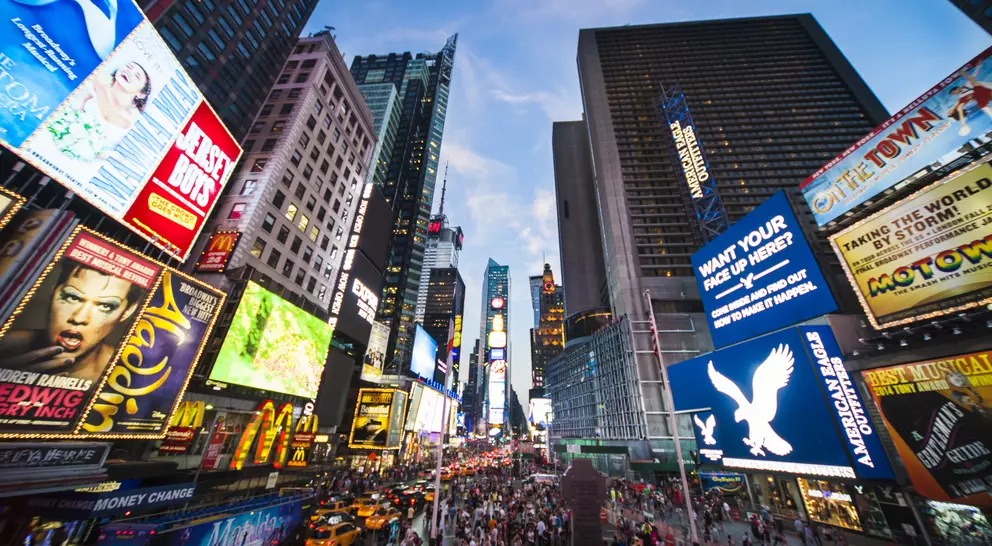 Tourists crossing Times Square surrounded by bright lights and advertisements