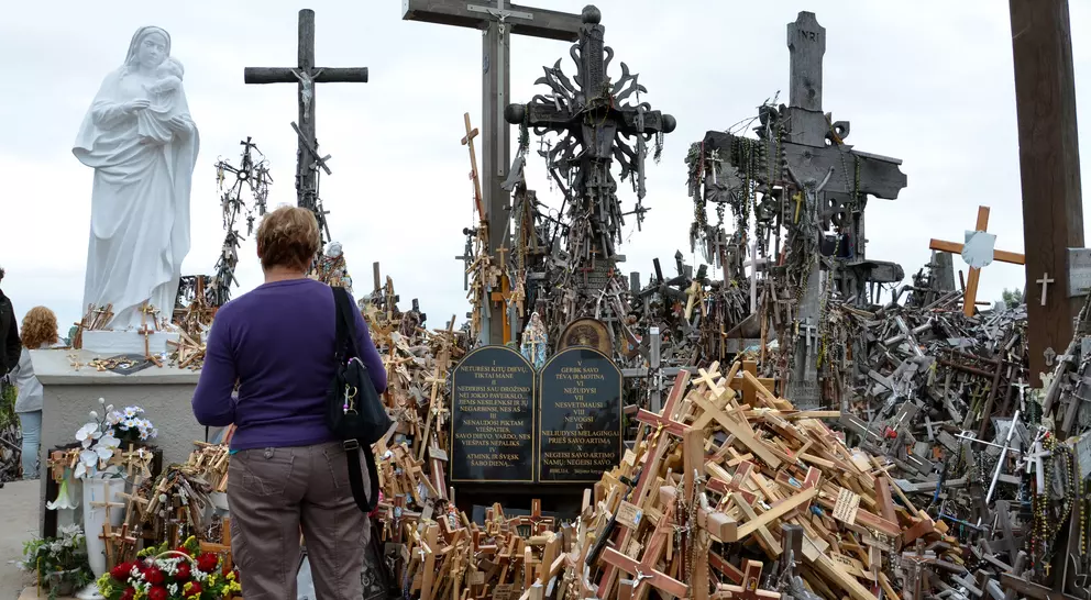 A woman stands before a shrine filled with wooden crosses and a statue, reflecting a memorial site.