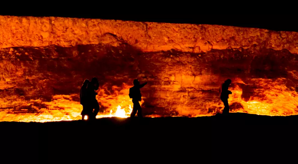 Silhouettes of people walking near a glowing, firelit rock wall at night.