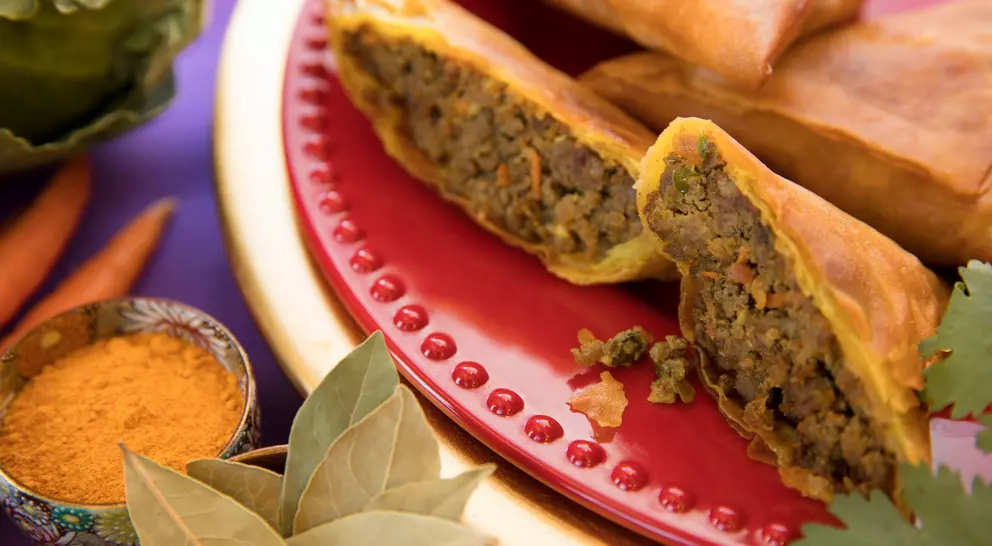 A plate of savory spring rolls filled with seasoned meat, surrounded by spices and fresh vegetables.