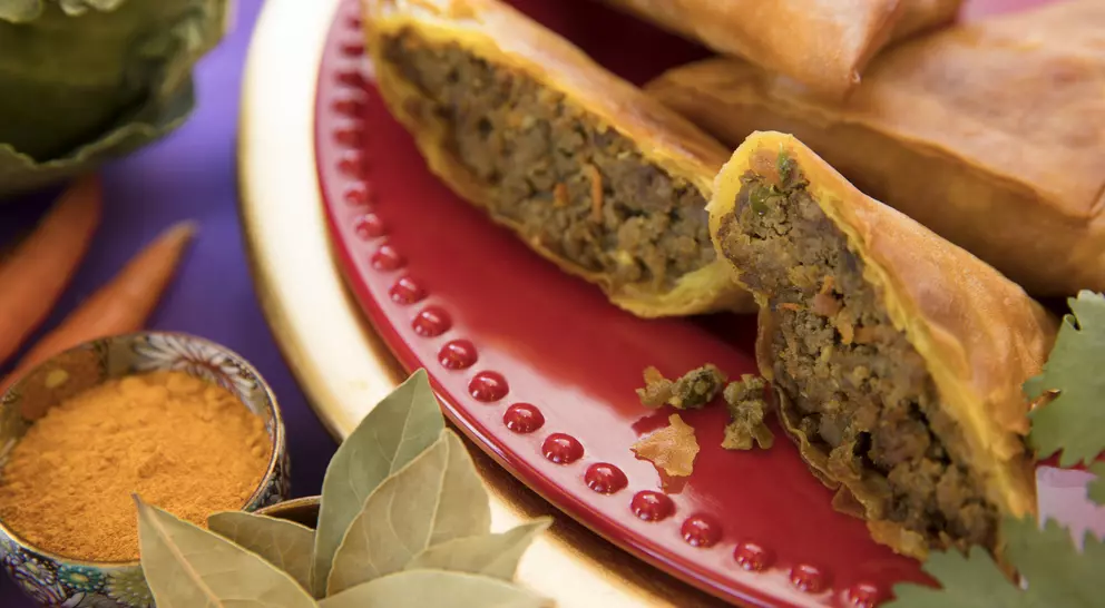 A plate of savory spring rolls filled with seasoned meat, surrounded by spices and fresh vegetables.