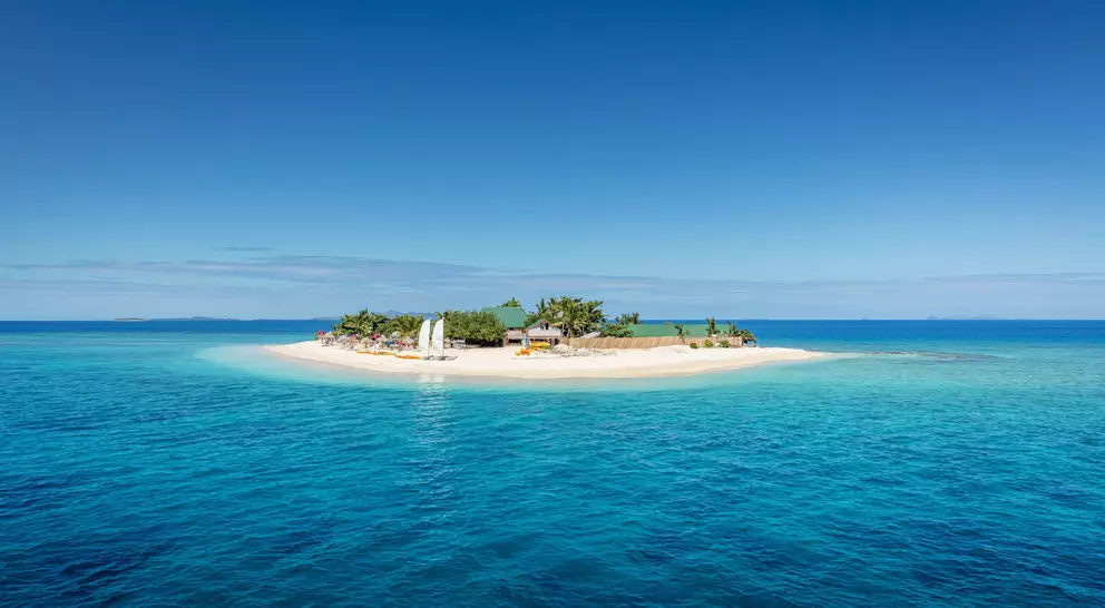 Beautiful small island in the middle of the south pacific ocean with beach huts, lounge chairs, palm trees, surrounded with beautiful clear turquoise water.