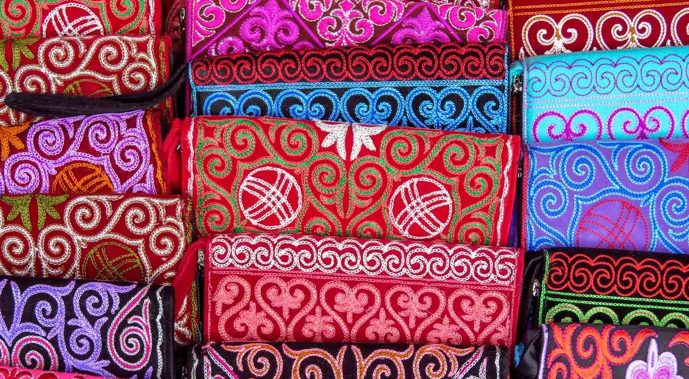 Colorful fabric pouches with intricate embroidery patterns in various shades of red, pink, blue, and black.