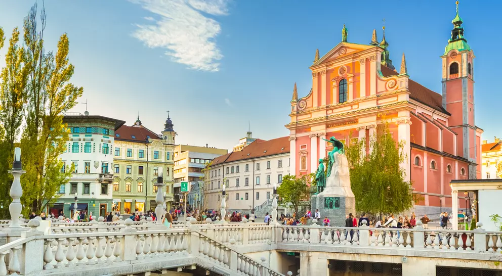 A scenic view of a bustling square with a bridge, colorful buildings, and a church under a clear blue sky.