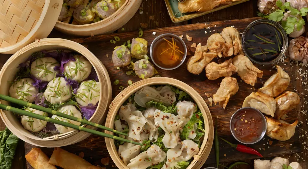 A spread of various Asian dumplings and spring rolls, served in bamboo steamers and accompanied by dipping sauces.