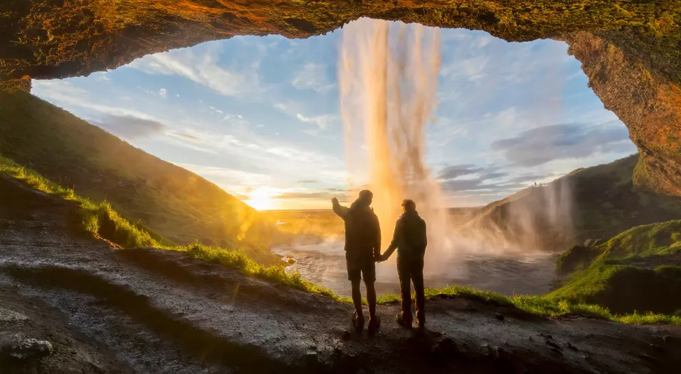 Tourists under waterfall in Seljalandsfoss, Iceland, man pointing with finger to the sun