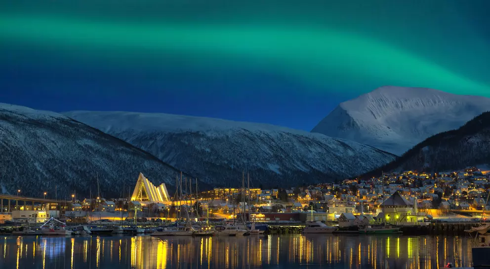 View at night on illuminated Tromso city with cathedral and majestic aurora borealis