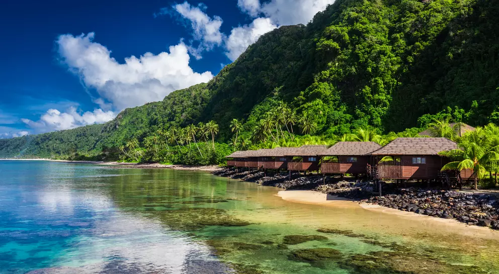 Small beach houses line the shore with green vegetation behind them
