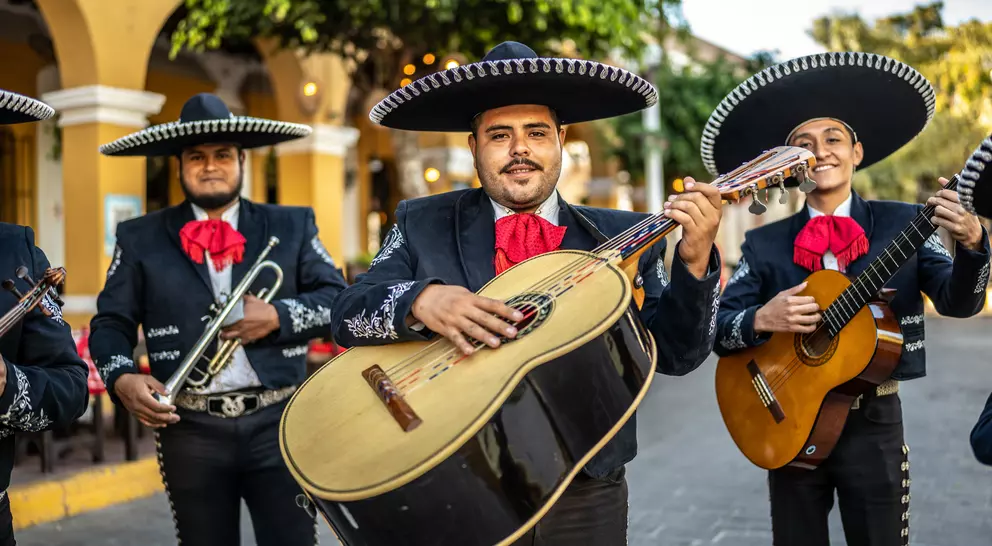 A group of Mexican mariachi musicians hold their instruments in an old town square.