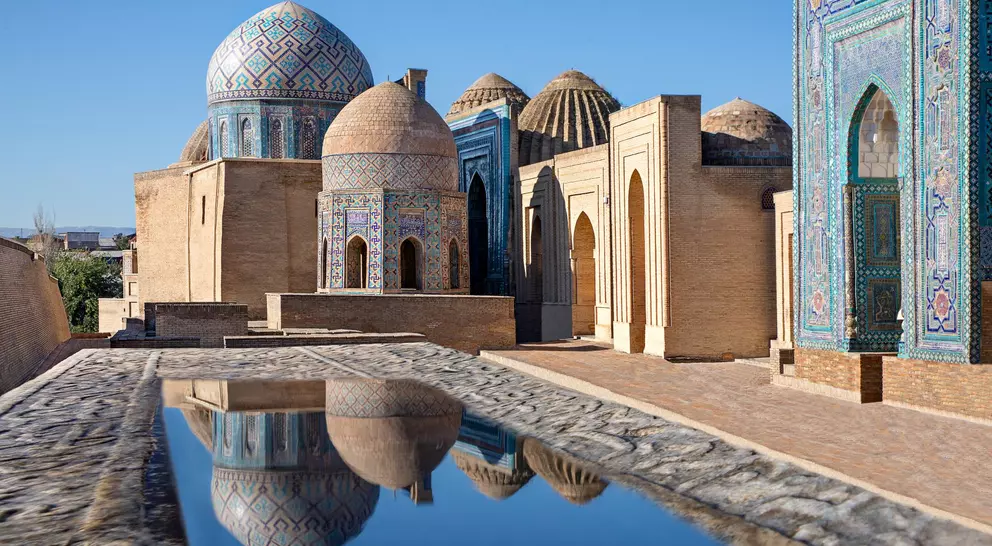Mausoleums and domes of the historical cemetery of Shahi Zinda and their reflections in puddle, Samarkand, Uzbekistan.