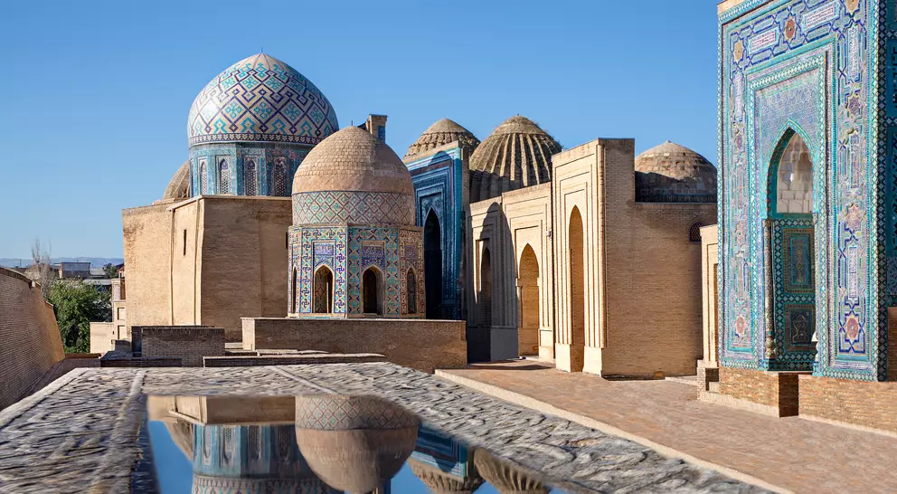 Mausoleums and domes of the historical cemetery of Shahi Zinda and their reflections in puddle, Samarkand, Uzbekistan.